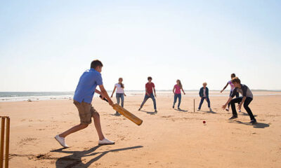 group of teenagers playing cricket on beach.